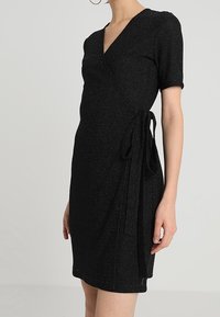 Schwarzes Wickelkleid aus strukturiertem Stoff, mit kurzen Ärmeln, tiefem V-Ausschnitt und einem gebundenen Taillenbereich für eine verstellbare Passform.