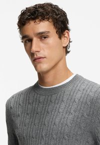 Grau gestrickter Pullover mit rundem Halsausschnitt, der ein strukturiertes Muster und gerippte Bündchen aufweist. Hergestellt aus weichem Material, enganliegendes Design.