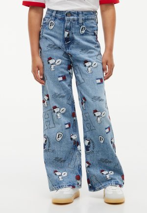Enfant portant un jean bleu à jambes larges avec des personnages Snoopy, des logos Tommy Hilfiger et des accents rouges, associé à des baskets blanches.