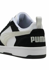 Sneaker in bianco e nero caratterizzato da materiali in suede e pelle, pannelli laterali testurizzati, una suola intermedia bianca e il logo ‘PUMA’ sul tallone.