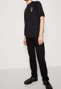 Svart sweatshirt med en djärv röd och vit ögondiagram, kombinerad med svarta jeans och glansiga svarta skor, med avslappnad passform och korta ärmar.