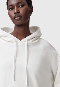 Sudadera blanca con cordón, con una textura suave y un corte relajado. Detalles de costura visibles y un diseño de capucha en capas.