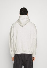 Lichtgrijze hoodie met een grote capuchon, verlaagde schouders en ribgebreide manchetten en zoom. Gemaakt van zachte, gestructureerde stof zonder zichtbare patronen.