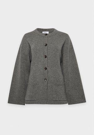 Un mannequin se tient devant un fond de studio blanc, portant un cardigan gris boutonné sur le devant, un pantalon à jambes larges et des sandales noires.
