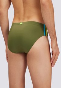 Grüne Schwimmbrief mit blauen und gelben seitlichen Streifen. Besitzt eine glatte Textur, ein eng anliegendes Design und ein kleines Logo-Detail auf der Rückseite.
