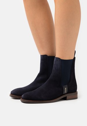 Navy suede ankle boots with elastic side panels, rounded toe, and a low wooden heel. Features a gold logo accent on the side.