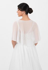 Sheer white overlay with a scalloped hem, layered over a white embroidered bodice. Elegant design with soft, flowing fabric.