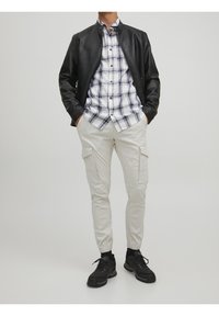 Musta nahkatakki, valko-siniraidallinen paita, vaaleanbeiget cargo-housut sivutaskuilla ja mustat karkeat lenkkitossut.