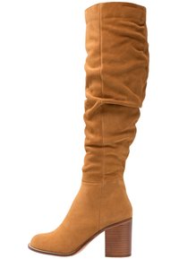 Botas de gamuza marrón, holgadas y por encima de la rodilla, con un tacón de madera grueso y un diseño de punta redondeada. Textura suave sin patrones visibles.