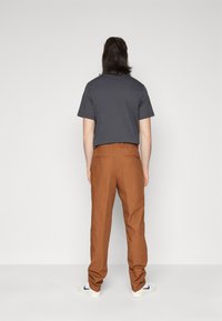 Brown cotton trousers with a straight leg design, back pockets, and a comfortable waistband, paired with a dark gray t-shirt.