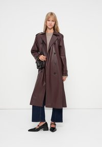 Burgundská umělá kožená trench coat s velkými klopami, dvouřadovým zapínáním a dlouhým střihem. V kombinaci s tmavými kratšími džíny a černými botami.