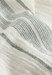 Tissu blanc avec un tissage texturé présentant de fines rayures horizontales noires et grises ainsi que des plis.