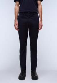 Navy slim-fit bukser lavet af bomuld, med knaplukning, forlommer og en glat tekstur. Båret med sorte sko.