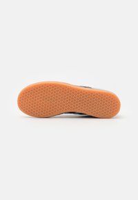 Black sneaker with a flexible, textured rubber sole featuring an orange bottom and a hexagonal pattern for grip.
