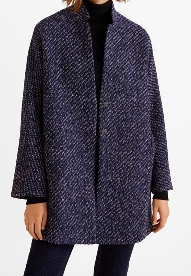 Femme portant un manteau ample en laine texturée bleu marine et gris avec deux boutons, associé à un col roulé noir et un pantalon foncé.