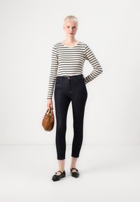 Sötétkék skinny farmernadrág, csíkos hosszú ujjú felső, fekete lapos cipő kiegészítőkkel és barna szőtt kézitáska. Minimalista dizájn, testhez simuló siluett.