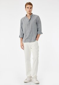 Grau-weiße gestreifte Hemdbluse mit langen, hochgerollten Ärmeln, kombiniert mit weißen Hosen und weißen Sneakern. Minimalistisches Design und weiche Textur.