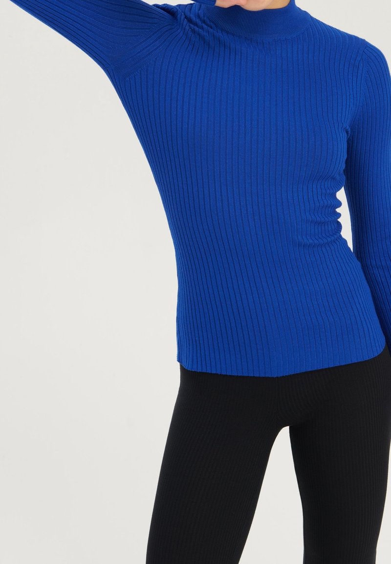 Haut à manches longues bleu côtelé avec un col montant, une silhouette ajustée et un motif tricoté texturé, associé à des leggings noirs côtelés.