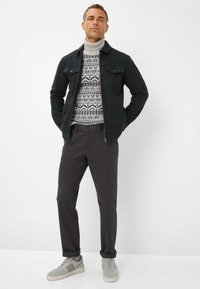 Giacca di lana verde scuro, maglione a collo alto grigio con fantasia, pantaloni grigio scuro e sneakers grigio chiaro dal design casual con risvolti.
