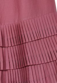 Jupe plissée en tissu rose doux avec des rayures texturées. Possède des volants superposés et des plis verticaux étroits pour un détail supplémentaire.