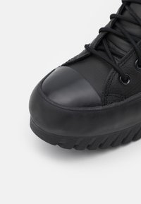 Czarny skórzany tenisówka z zaokrąglonym noskiem, gumową nakładką i teksturowaną podeszwą. Posiada czarne sznurówki i przeszycia na cholewce.