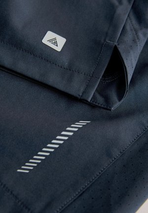 Tmavomodré športové šortky s hladkým povrchom, prešitými okrajmi, logom a reflexnými diagonálnymi pruhmi na zvýšenie viditeľnosti.