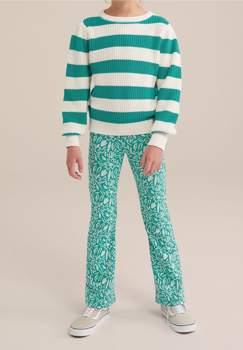 Enfant portant un pull à rayures bleu sarcelle et blanc, un pantalon à motifs floraux bleu sarcelle et des baskets beige sur fond beige.