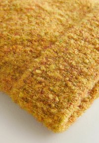 Wollstrickstoff in Gelb- und Orangetönen, texturiert mit einer flauschigen, geschlungenen Oberfläche, die sichtbare, unterschiedliche Garnstränge aufweist.