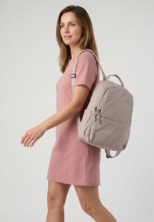 Vrouw in een roze jurk die loopt en een lichtgrijze rugzak met meerdere ritsvakken op haar schouder draagt.