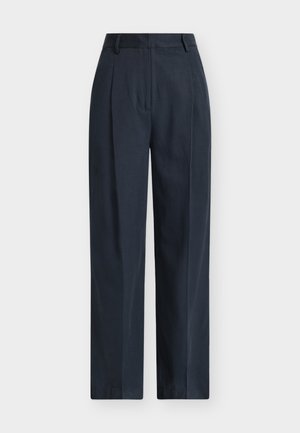 Pantalons larges bleu marine en tissu léger, avec plis à l'avant, poches latérales, et texture lisse. Détail de ceinture sur mesure.