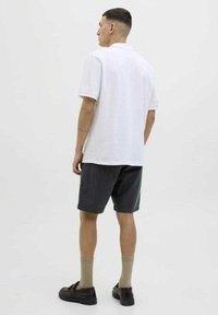 Polo shirt bianco, pantaloni corti scuri, scarpe marroni, calzini beige. Design semplice, maniche corte, colletto standard, taglio aderente, texture del tessuto morbida.