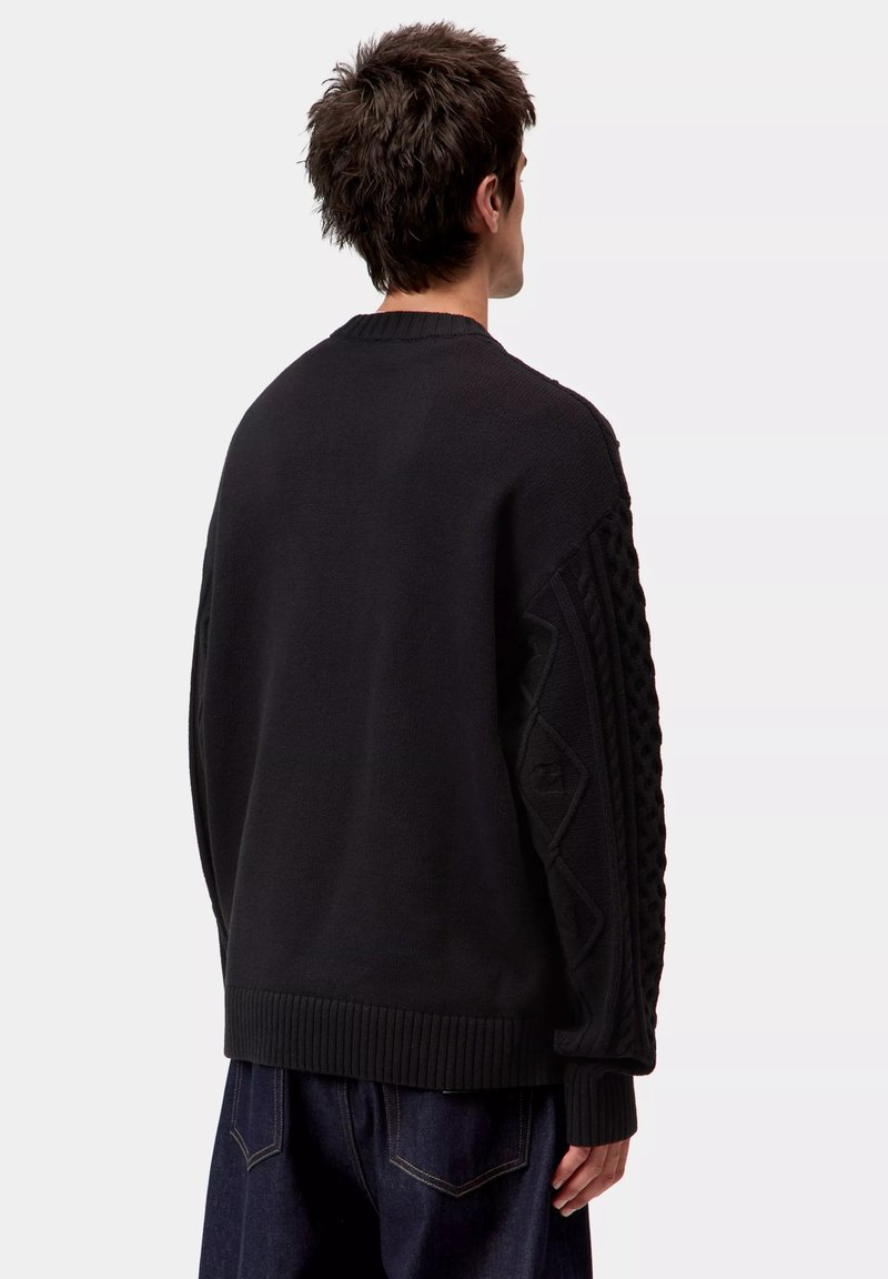 Jersey negro de punto con mangas texturizadas, cuello redondo y dobladillo acanalado. Presenta patrones geométricos en los hombros y las mangas.