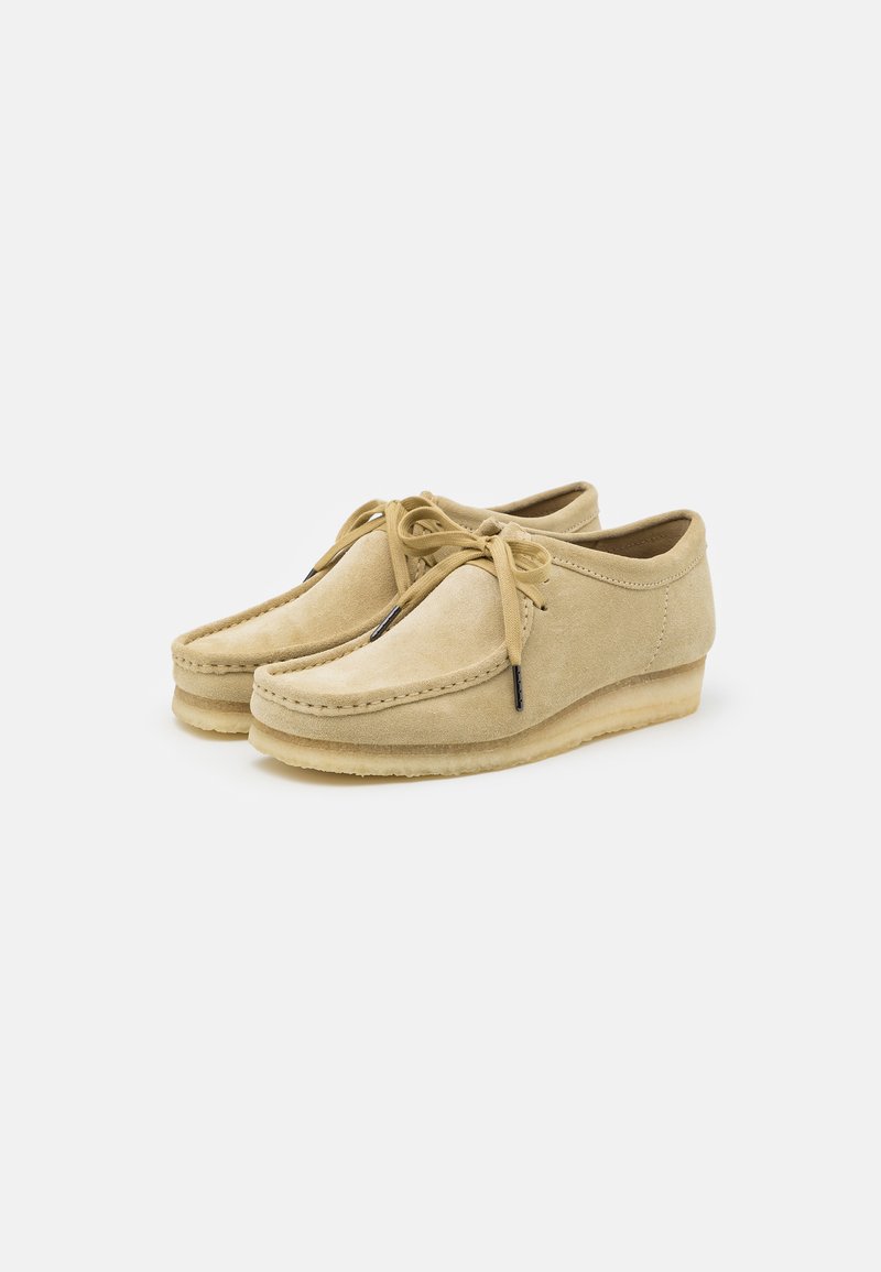 Scarpe in suede beige con punta arrotondata, design con lacci e suola imbottita. Dettagli di cucitura sottili lungo i bordi e una consistenza liscia.