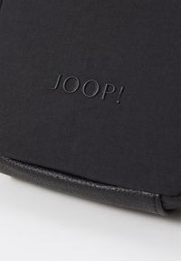 Borsa di stoffa nera con un fondo in pelle testurizzata. Il nome del marchio "JOOP!" è impresso sulla parte frontale con una finitura opaca e discreta.