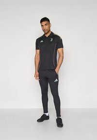 Polo atletica nera con dettagli rosa, con colletto e maniche corte. Abbinata a pantaloni neri aderenti, con il marchio Adidas.