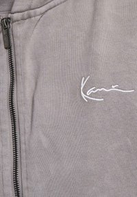 Gray zip-up hoodie featuring a textured fabric, black zipper, and white embroidered logo on the left chest area.