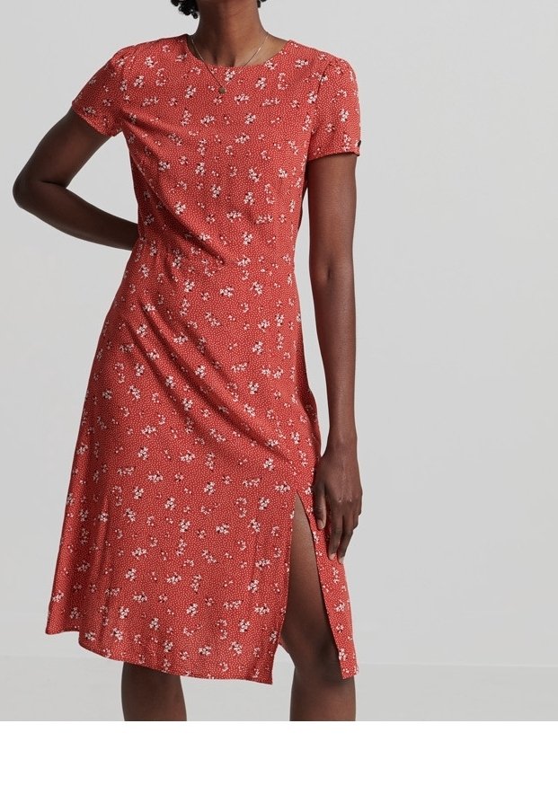 Femme portant une robe rouge à manches courtes, longueur genou, avec de petits motifs floraux blancs et une fente latérale montant jusqu'à la cuisse.