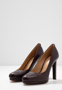 Dark brown leather high-heeled shoes with rounded toe, smooth texture, and a wooden-textured heel. Simple design, no visible patterns or accents.