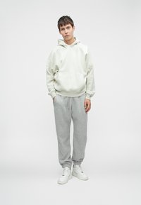 Lys grå hettegenser med kengurulomme og stjernemønster på ermene, kombinert med lys grå joggebukser og hvite høyhælte sneakers.