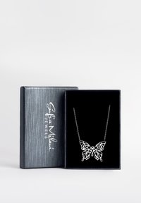 Silverfärgad fjärils halsband med intrikat utskuren design, visad på en svart bakgrund inuti en texturerad grå smyckeslåda.