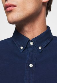 Mörkblå knappar med skjorta med en strukturerad krage, med två vita knappar och en texturerad tyg. Nära bild av halsområdet.