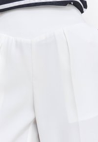 Białe spodnie z plisowanej tkaniny o gładkiej fakturze, z wysokim stanem i subtelnym połyskiem. Projekt oferuje czysty, minimalistyczny wygląd.