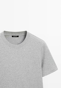 Šedé bavlněné tričko s kulatým výstřihem a krátkými rukávy. Obsahuje prošitý lem a malou černou nášivku na krku.