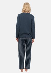 Marinblå långärmad topp med rund halsringning, matchad med randiga, avslappnade byxor. Materialet verkar mjukt med en slät yta.