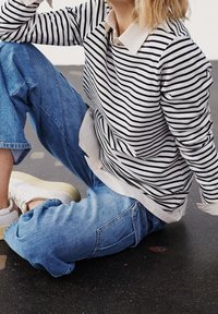Camisa de manga larga a rayas en blanco y azul marino, superpuesta sobre una camisa de cuello, combinada con unos vaqueros holgados de color azul claro y zapatillas blancas.