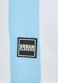 Helles Blau und weiße Stoff mit einem rechteckigen schwarzen Etikett, das "URBAN CLASSICS" in fetter weißer Schrift zeigt. Glatte Textur.