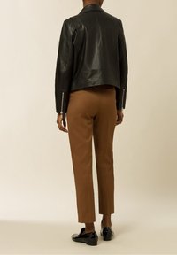 Svart läder mopedjacka med en cropped design, silverfärgade dragkedjor på ärmarna, tillsammans med skräddarsydda bruna byxor och svarta loafers.