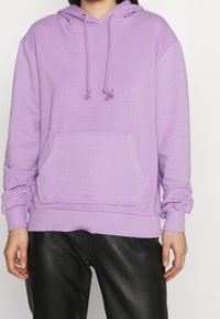 Lavendelfarbener Hoodie mit Kordeln, einer vorderen Tasche, gerippten Bündchen und Saum. Das Material wirkt weich und strukturiert und ist für die Freizeit gedacht.