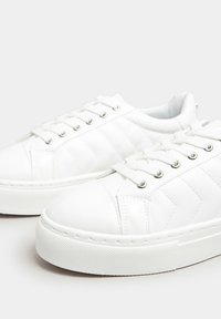 Zapatillas blancas con un material suave similar al cuero, que presentan un diseño acolchado en forma de diamante, puntera redonda y suela de goma con agarre texturizado.