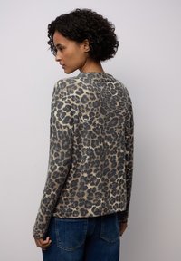 Leopardo-mönstrad stickad tröja med rund halsringning, långa ärmar och mjuk textur; har en öppen ryggdesign och avslappnad passform, i kombination med jeans.